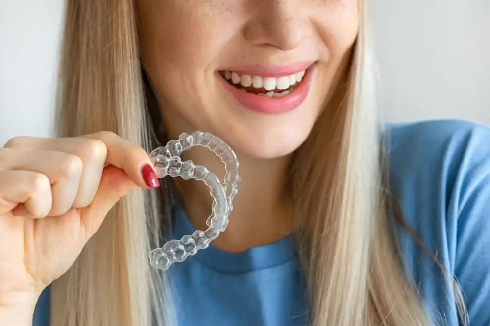 Clear aligner tray being held up beside a smile